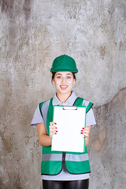 프로젝트 시트를 시연하는 녹색 유니폼과 헬멧을 쓴 여성 엔지니어