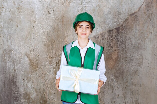 Free photo female engineer in green uniform and helmet holding a blue gift box