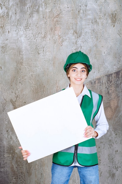 Foto gratuita ingegnere donna in uniforme verde e casco in possesso di un pannello informativo rettangolare