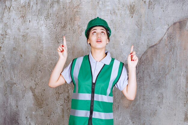 Female engineer in green uniform and helmet pointing above with emotions