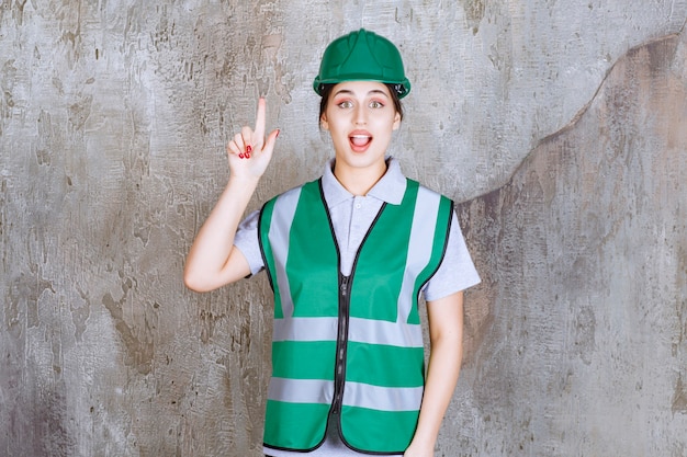 Female engineer in green uniform and helmet pointing above with emotions