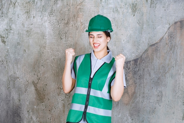 Female engineer in green uniform and helmet showing her fists and feeling positive