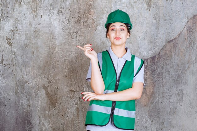 Женщина-инженер в зеленой форме и шлеме показывает левую сторону с эмоциями
