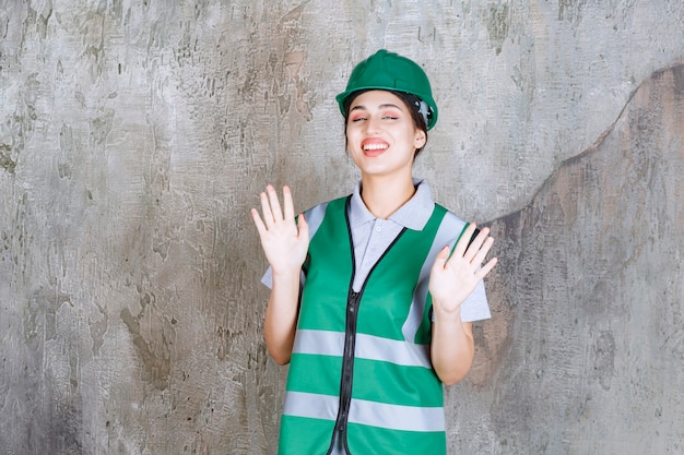 Female engineer in green uniform and helmet stopping something. 