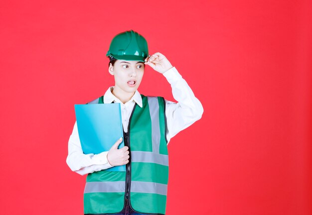 Female engineer in green uniform holding a blue folder and looks scared and terrified