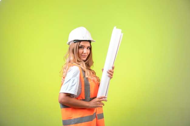 Female engineer in helmet and gear holding the construction plan and looks confident.