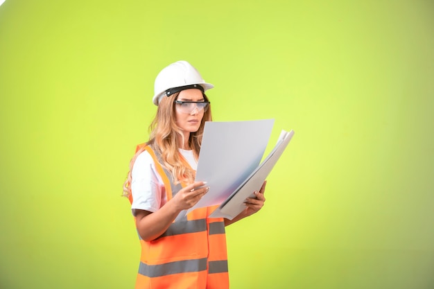 Female engineer in helmet and gear holding project plan and correcting it.