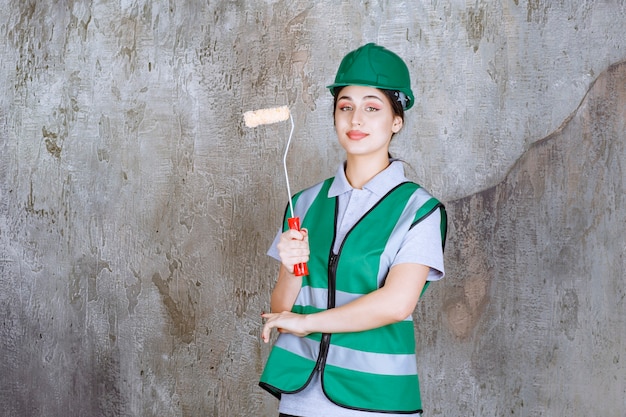 無料写真 壁の絵のトリムローラーを保持している緑のヘルメットの女性エンジニア