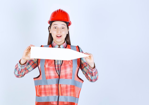 Female engineer in red helmet holding an arrow pointing to the right.