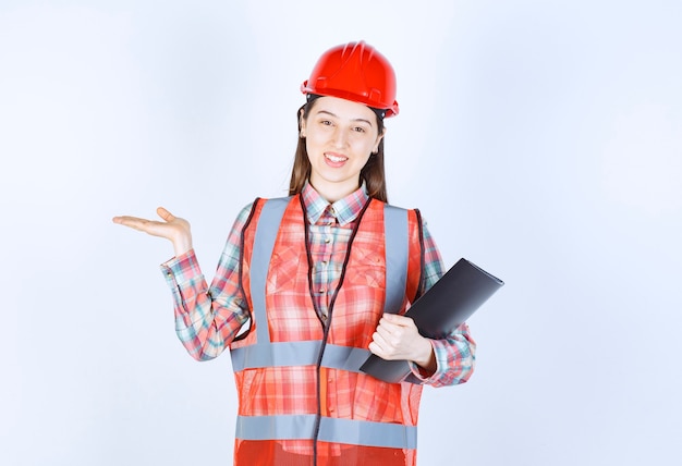 Free photo female engineer in red helmet holding a black project plan.