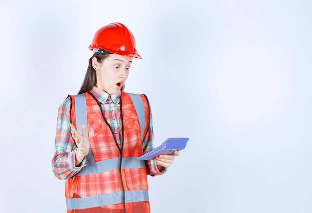 Female engineer in red helmet working on calculator and looks confused or thrilled.