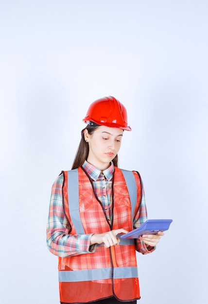 Female engineer in red helmet working on calculator.