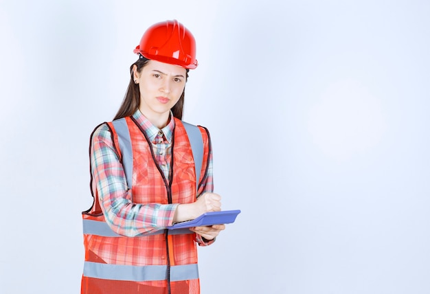 Female engineer in red helmet working on calculator.