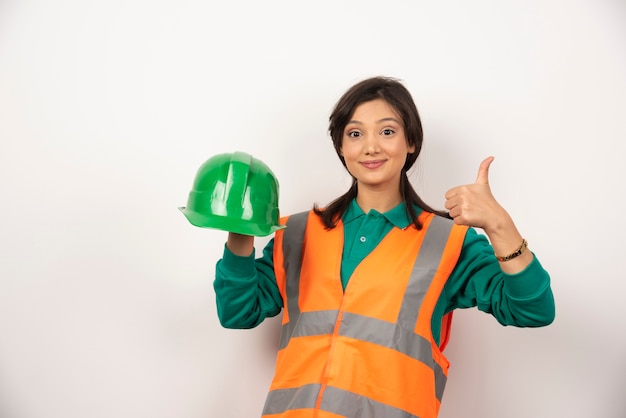 Female engineer showing thumb up and holding a helmet on white background