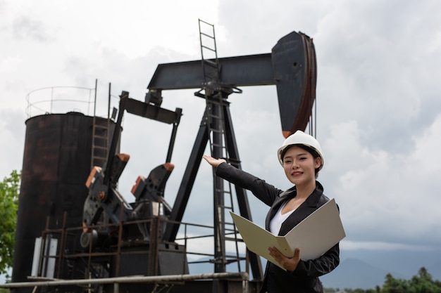 Female engineer standing beside working oil pumps with a sky .