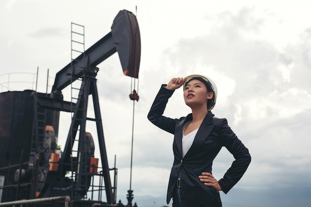 Free photo female engineer standing with working oil pumps with a white sky .