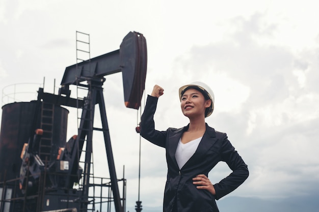 Female engineer standing with working oil pumps with a white sky .