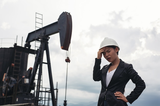 Female engineer standing with working oil pumps with a white sky .