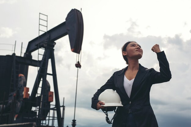 Female engineer standing with working oil pumps with a white sky .