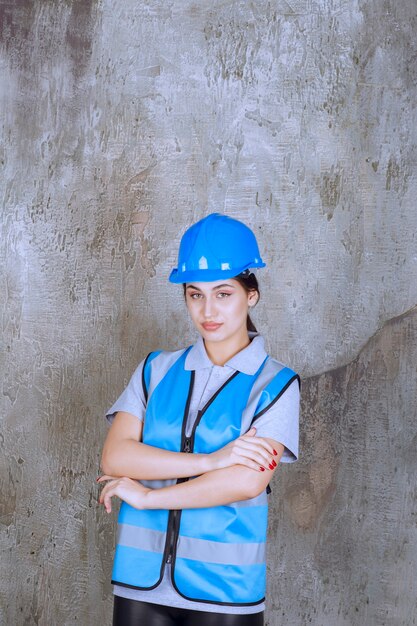 파란색 헬멧과 장비를 착용하고 팔짱을 끼고 전문적인 포즈를 취하는 여성 엔지니어.