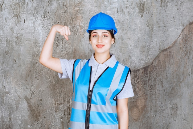 Foto gratuita ingegnere femminile che indossa casco blu e attrezzi e mostra il suo muscolo del braccio.