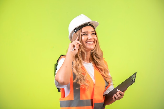 Ingegnere femminile in casco bianco e attrezzi che tengono la lista di controllo e il pensiero.