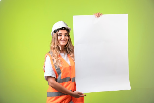 Female engineer in white helmet and gear showing the construction plan and the standards.