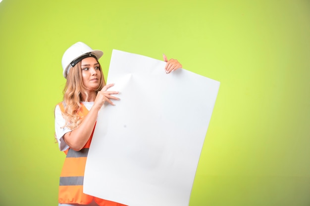 Женский инженер в белом шлеме и шестерне, показывая план строительства.