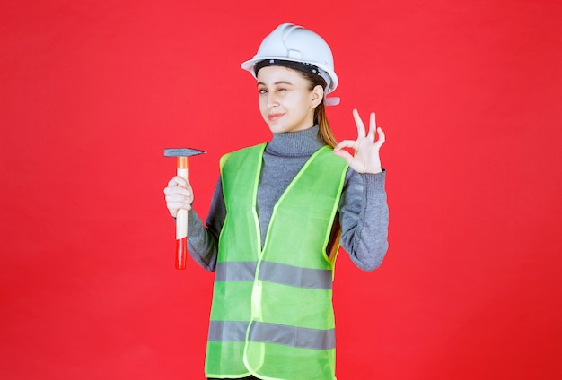 Female engineer with white helmet holding a wooden ax and showing enjoyment hand sign. 