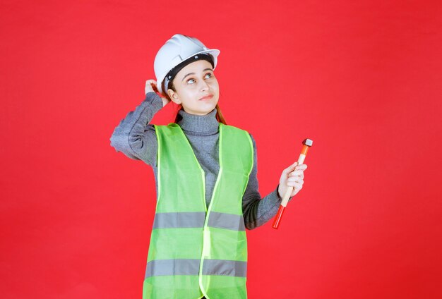 Female engineer with white helmet holding a wooden ax and thinking of how to use it. 