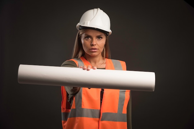 Ingegnere femminile con un casco bianco che offre il piano del progetto.