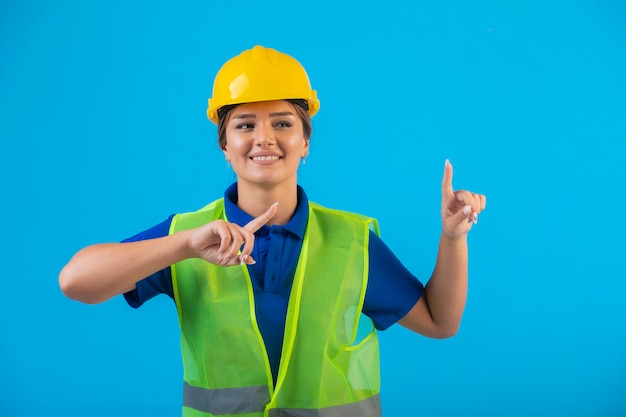 Female engineer in yellow helmet and gear pointing up.