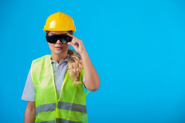 黄色いヘルメットとギアを身に着けている女性エンジニアは、プロを装った光線予防眼鏡をかけています。