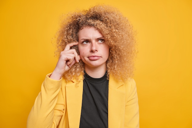 female entrepreneur in formal clothes scratches temples tries to remember important information comes up with ideas poses indoor