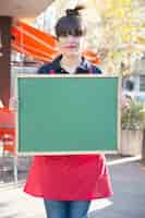 Free photo female entrepreneur holding blank green menu board at outdoors caf�
