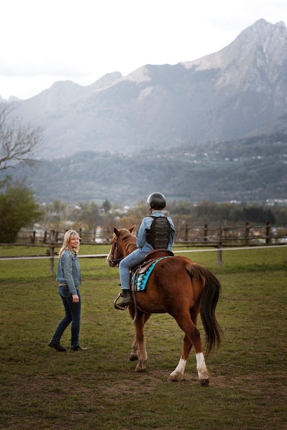 Foto gratuita istruttore equestre femminile che insegna al bambino come andare a cavallo