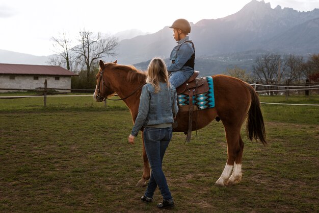 Женщина-инструктор по верховой езде учит ребенка кататься на лошади