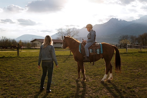 Free photo female equestrian instructor teaching child how to ride horse