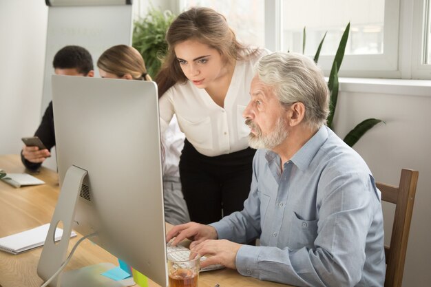 Женский исполнительный учить старшего работника офиса помогая объяснять работу компьютера