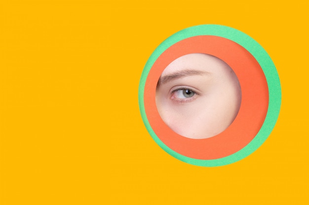 Женский глаз смотрит, выглядывает через круг в оранжевом фоне
