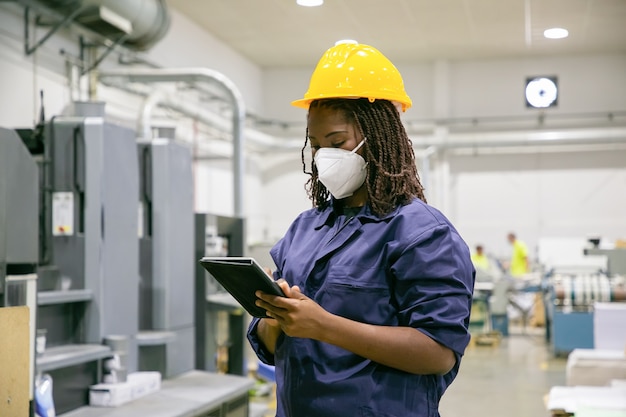 Female factory worker in mask holding tablet