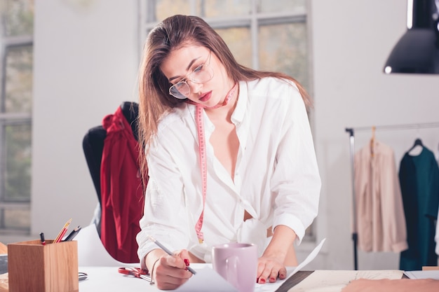 Foto gratuita la stilista femminile che lavora nella seduta sulla scrivania