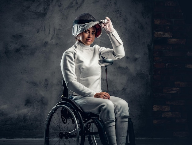 Female fencer in wheelchair holds safety mask and a sword.