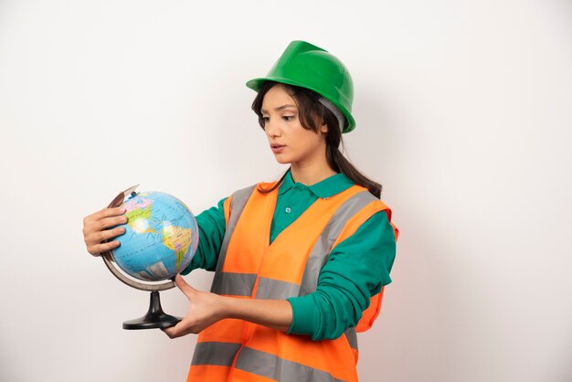 Female firefighter looking at globe with serious expression on white background.