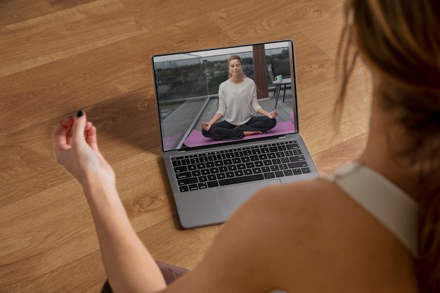 Женщина-инструктор по фитнесу преподает йогу из дома через ноутбук
