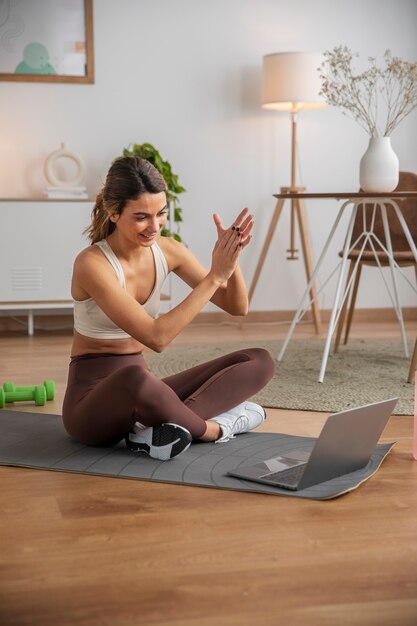 Женщина-инструктор по фитнесу использует ноутбук для проведения занятий из дома