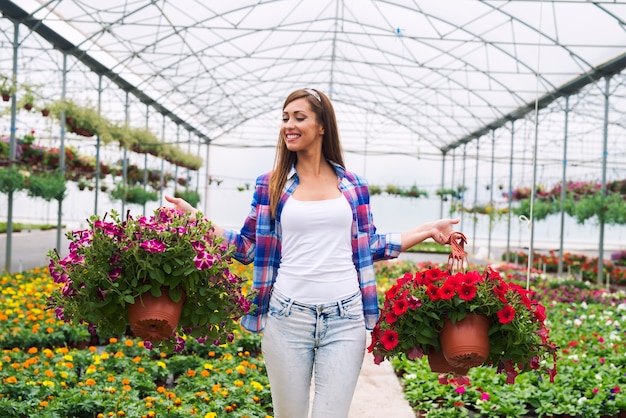 温室で鉢植えの花の植物を運んで販売のためにそれらを配置する女性の花屋