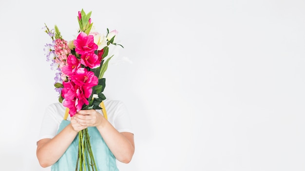 Female florist hiding her face behind bunch of flowers on white background