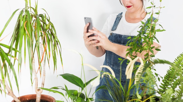 Женский цветовод с фотографией растений в горшках на смартфоне