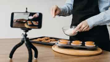 Foto gratuita blogger di cibo femminile in streaming a casa con lo smartphone durante la cottura